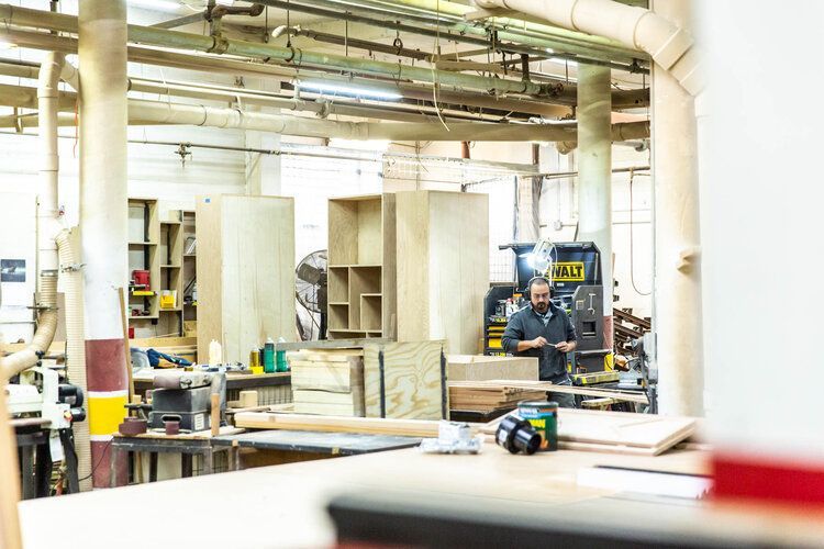 A man is standing in a woodworking factory looking at his phone.