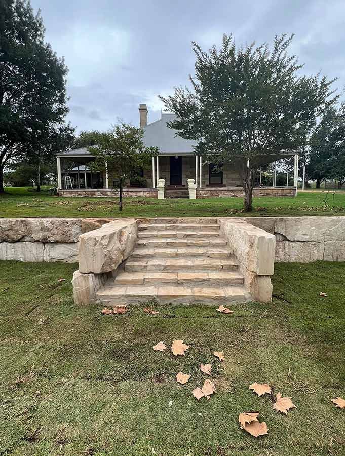 A House With Stairs Leading Up to It is Sitting on Top of a Lush Green Field — B & C Yard Improvements in Dubbo, NSW