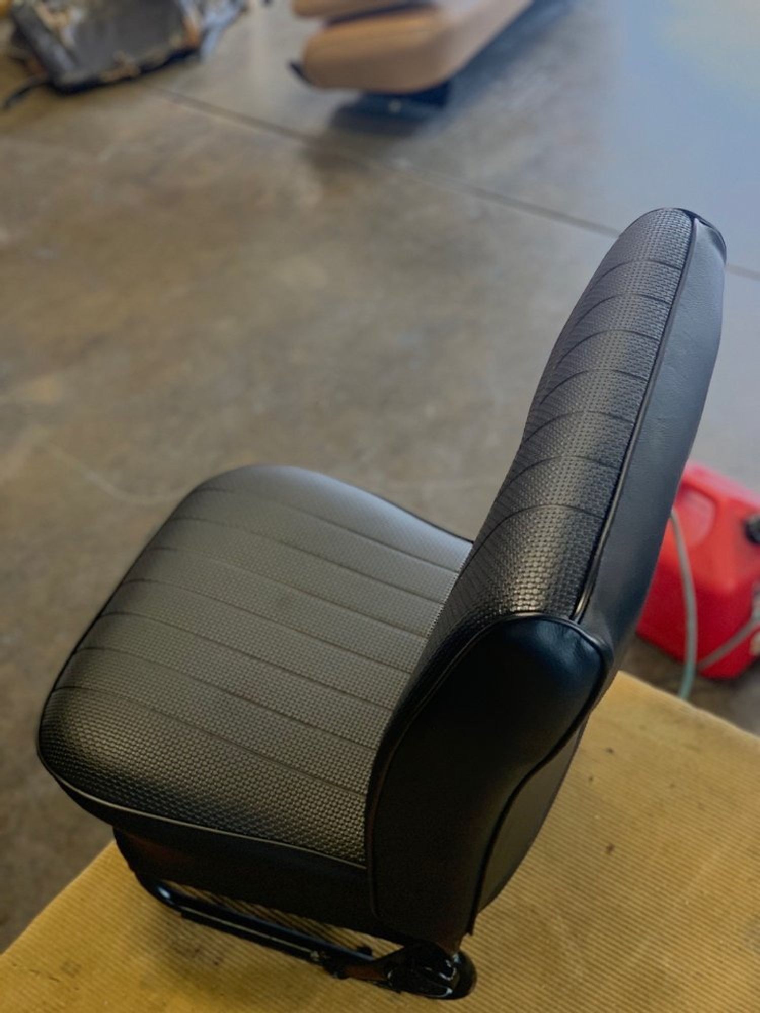 Black car seat with vertical stitching, metal frame, in a workshop.