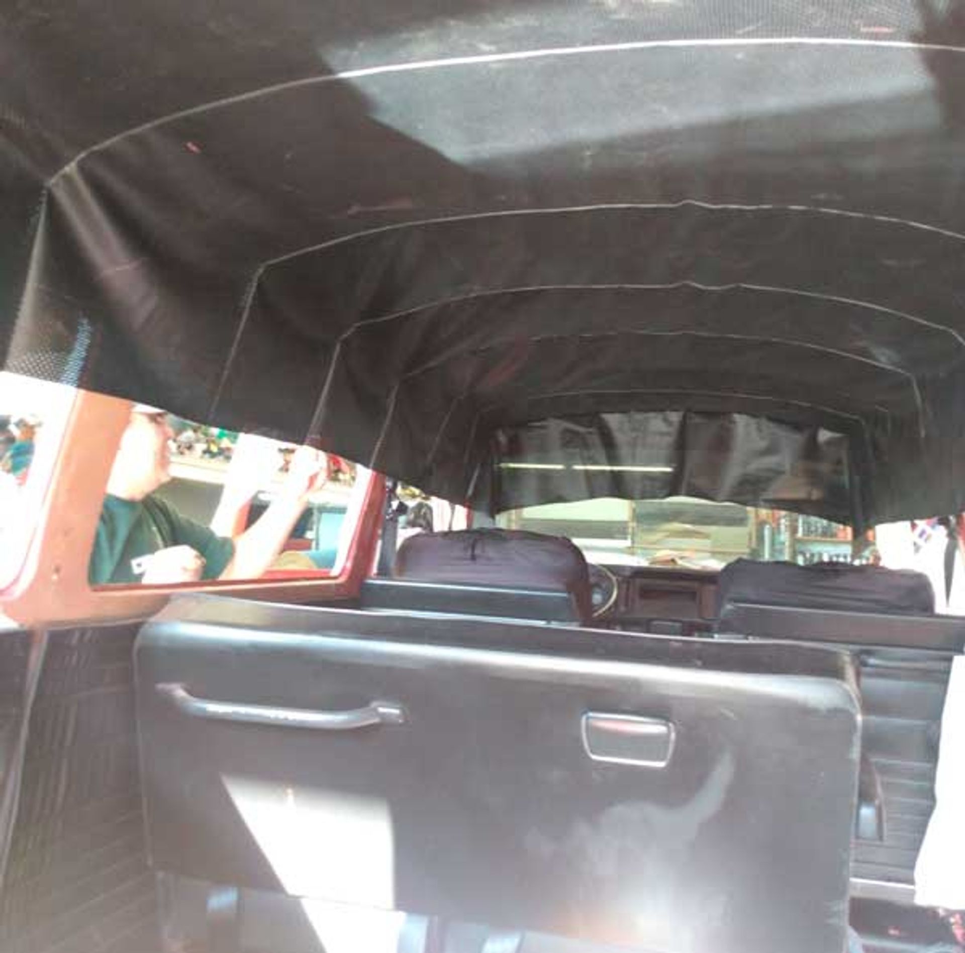 Interior view of a vintage vehicle with dark seats, a black canopy, and a person looking out a side window.