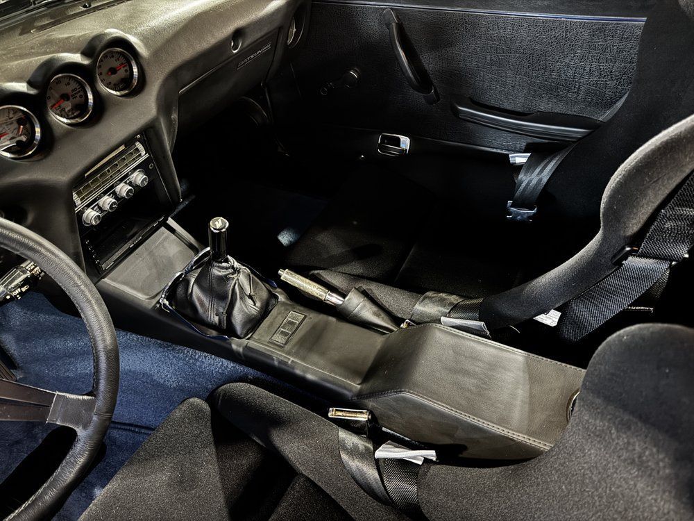 Black car interior, center console and racing seats, steering wheel in frame, with gauges.