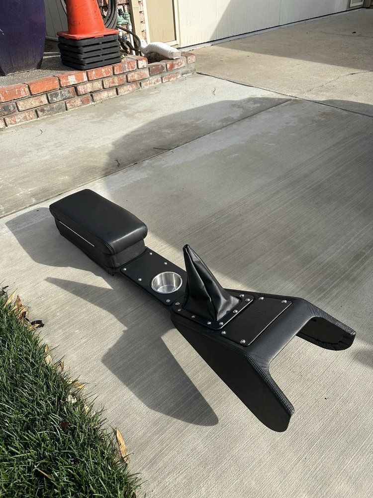 Black custom car console with cup holders and shift boot on a concrete driveway.