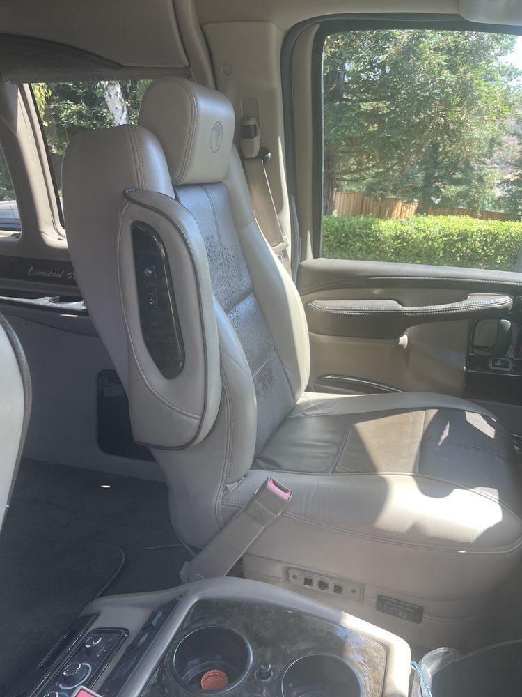 Tan leather interior of a van with a captain's chair, armrest with controls, and cup holders.