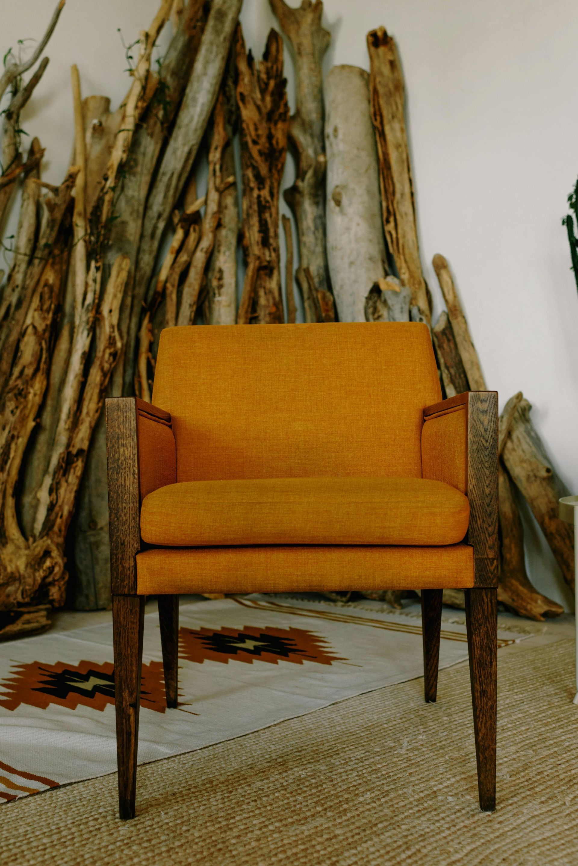 Orange upholstered armchair with wood frame, driftwood background.
