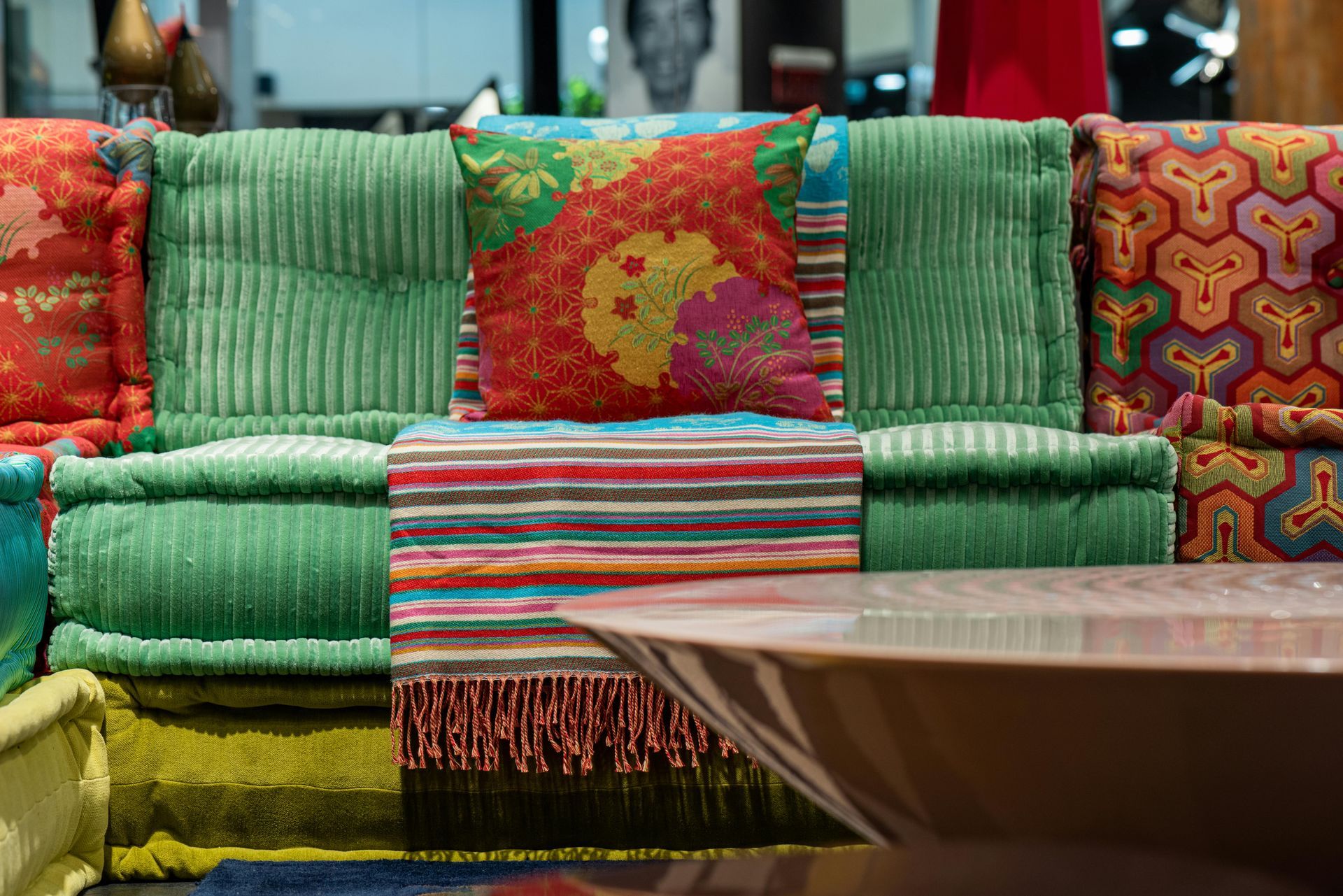 Colorful cushions in a sofa-like setting with a patterned central pillow and a table in the foreground.