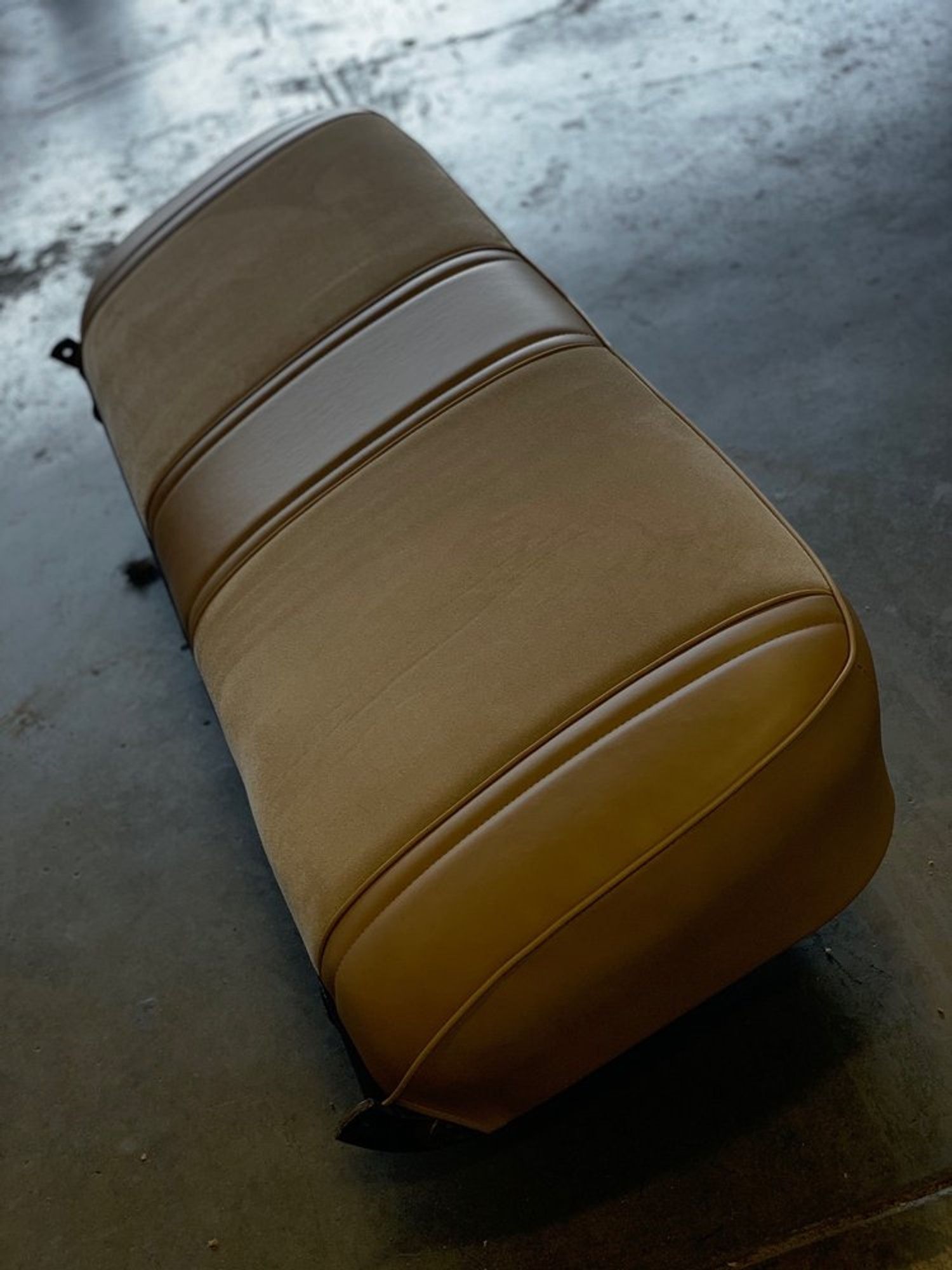 Tan car seat back with brown stripe and trim on a dark floor.