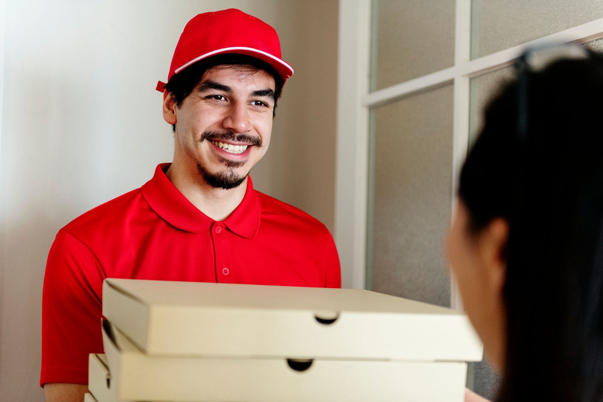 A person in a red uniform holding a box | Online Pizza Delivery
