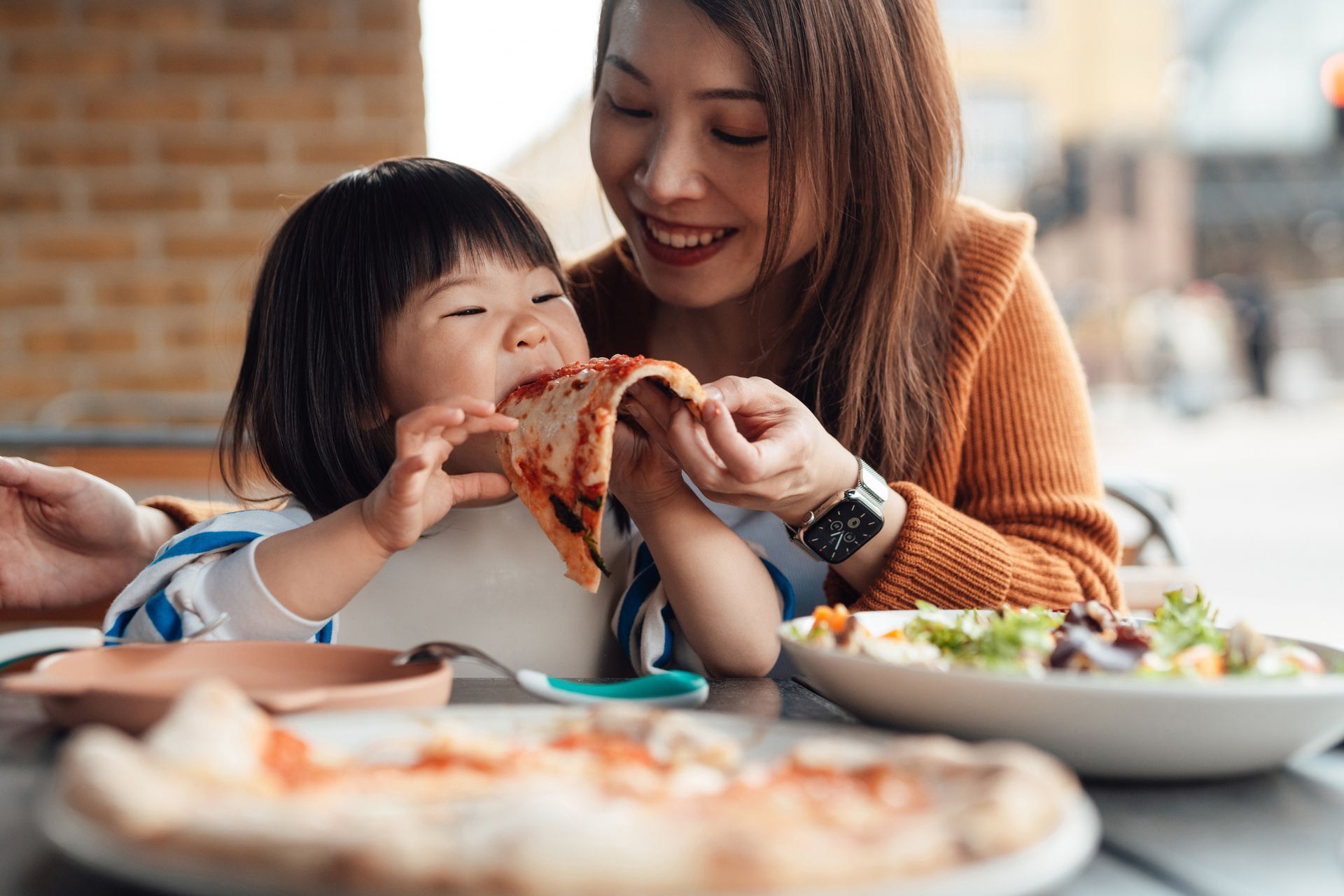 A mom is giving her daughter a slice of pizza. A mom is giving her daughter a slice of pizza.