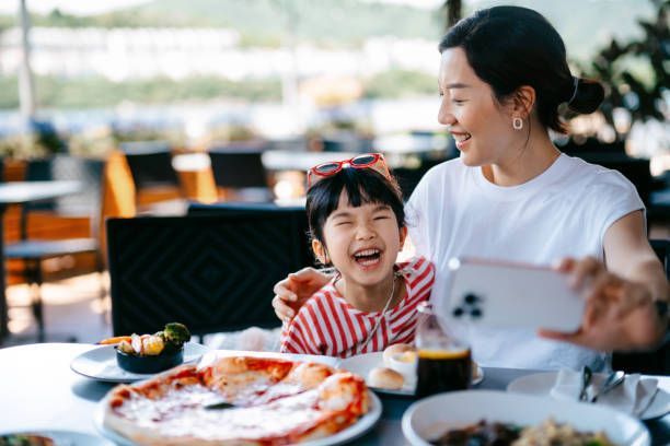 A mother is taking a selfie with her daughter in a pizzeria.