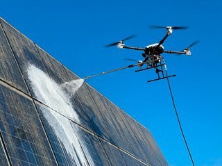 Un drone survole un bâtiment en briques, avec des câbles reliés au toit.