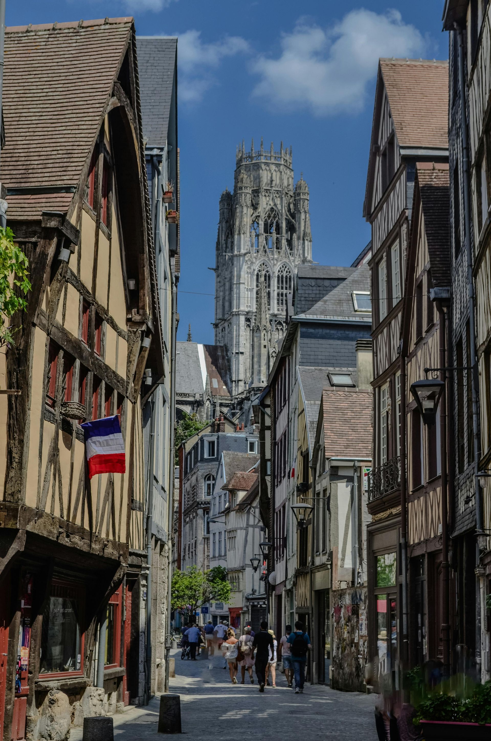 Rue étroite de Rouen, en France, bordée de bâtiments à colombages et apercevant au loin le clocher d'une cathédrale