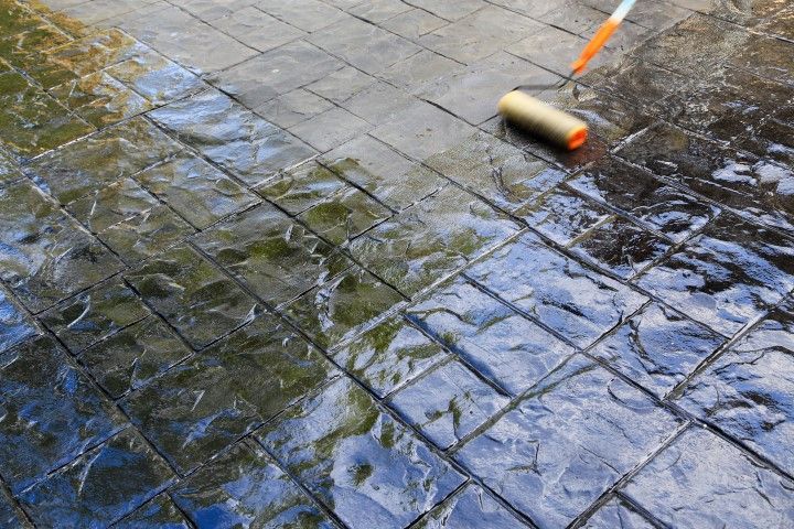 Paint roller applying coating to a wet, dark tiled pavement reflected in water