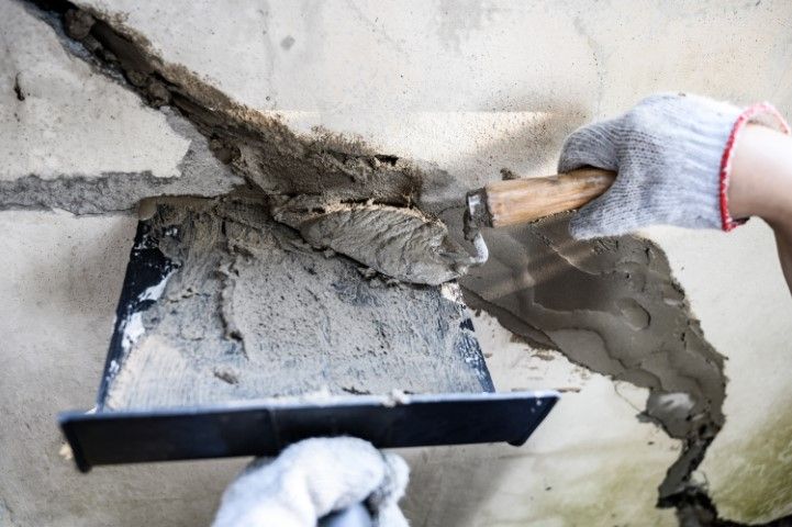 Worker smoothing wet cement on a wall with a trowel and hawk tool