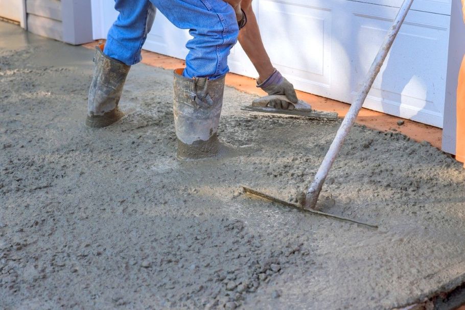 Workers smoothing wet concrete at a construction site with a trowel and boots.