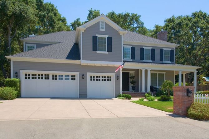 Suburban two-story house with blue-gray siding, white trim, and a three-car garage under a clear sky