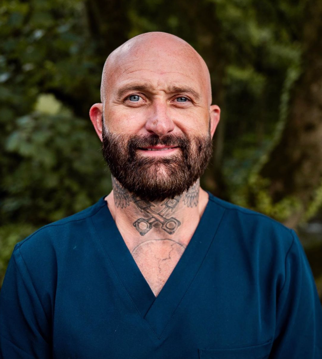a bald man with a beard and tattoos on his neck is wearing a blue scrub top .