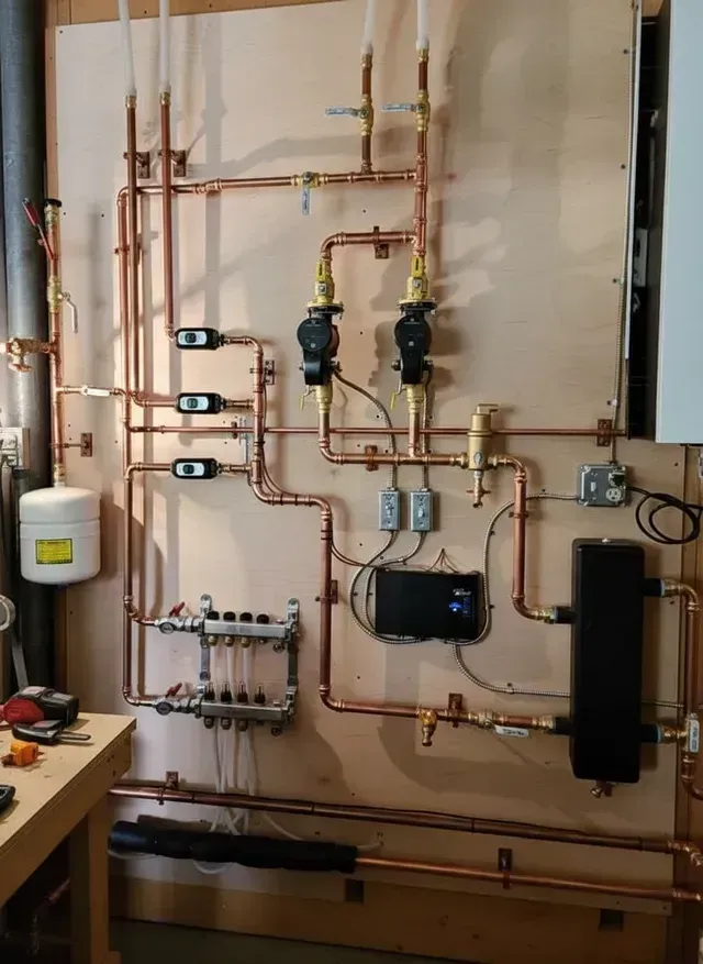 A neatly arranged residential hydronic heating system with copper piping, pumps, and a digital controller on a wood wall.