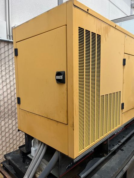 Yellow generator in an outdoor setting with a metal cage fence.