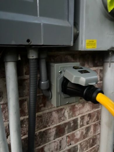 Outdoor electrical outlet with a yellow extension cord plugged in, mounted on a brick wall.