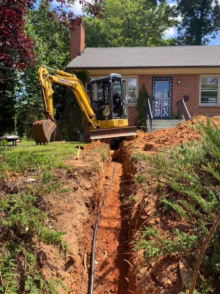 A small excavator digging a trench in front of a brick house.