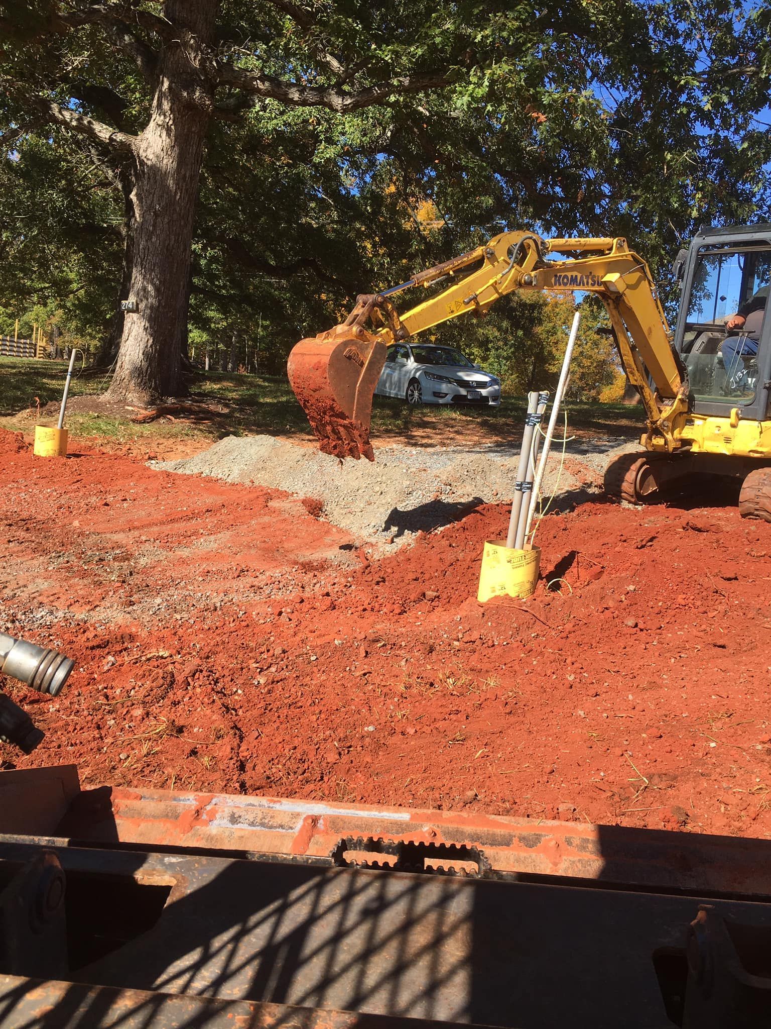 Yellow excavator digging in red dirt; tree in background.