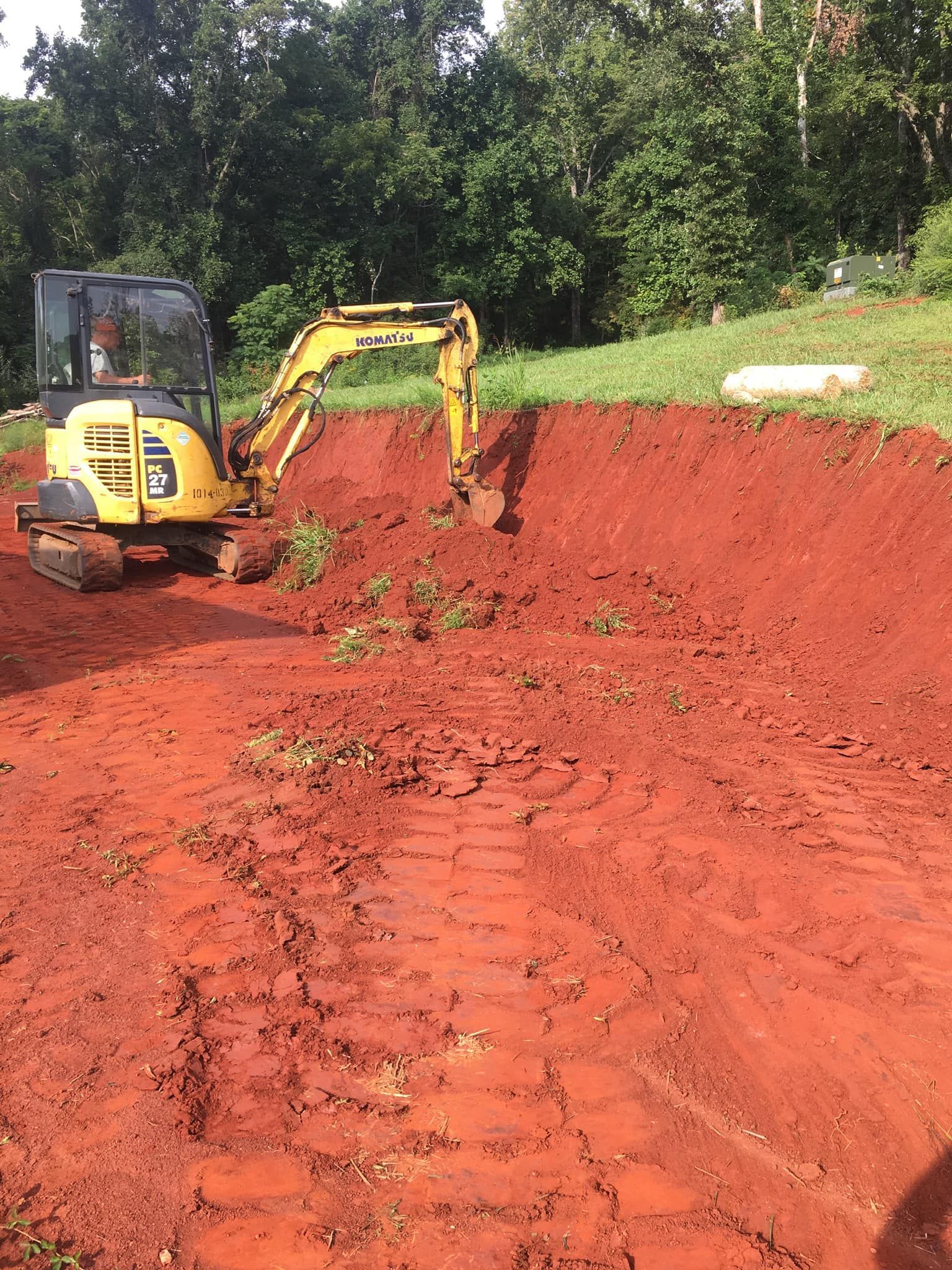 Yellow excavator digging in red soil on a hillside.
