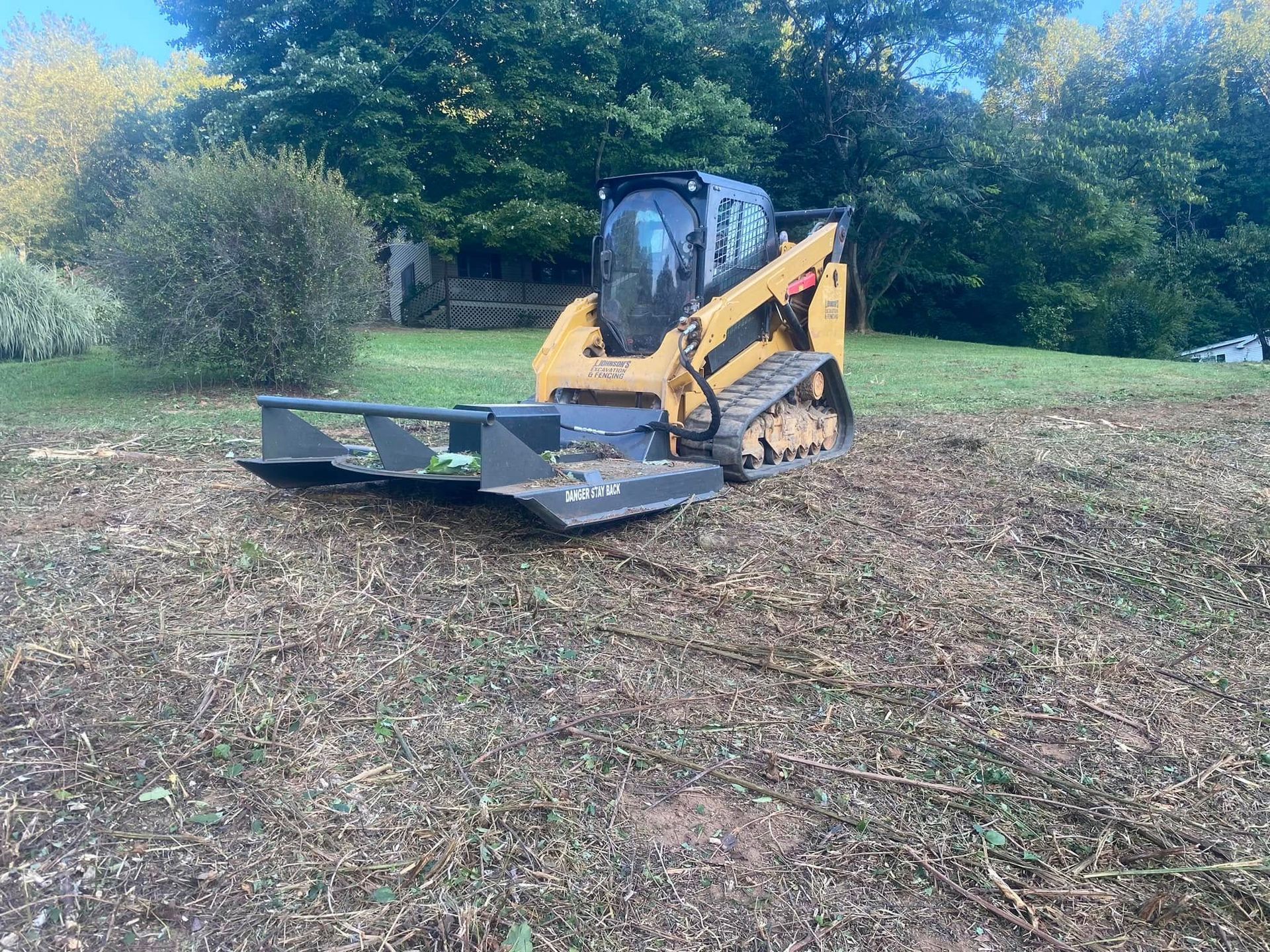 Yellow and black skid steer on tracks with brush cutter attachment on a mulched area.