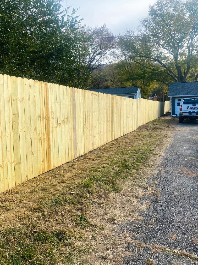 Wooden fence running along a gravel driveway; grass and trees in the background.