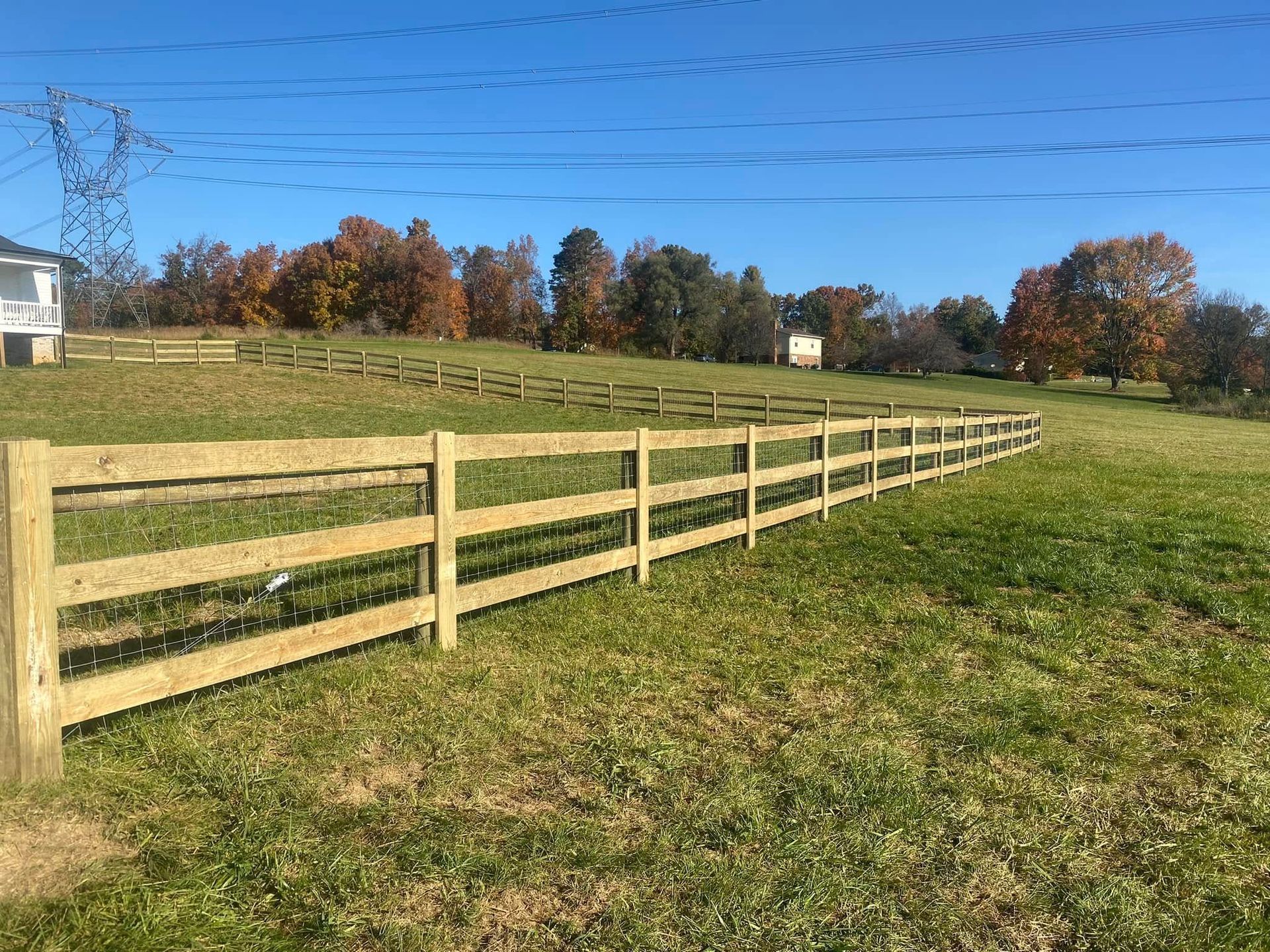 Wooden fence in a grassy field on a sunny day. Trees in the background, blue sky.