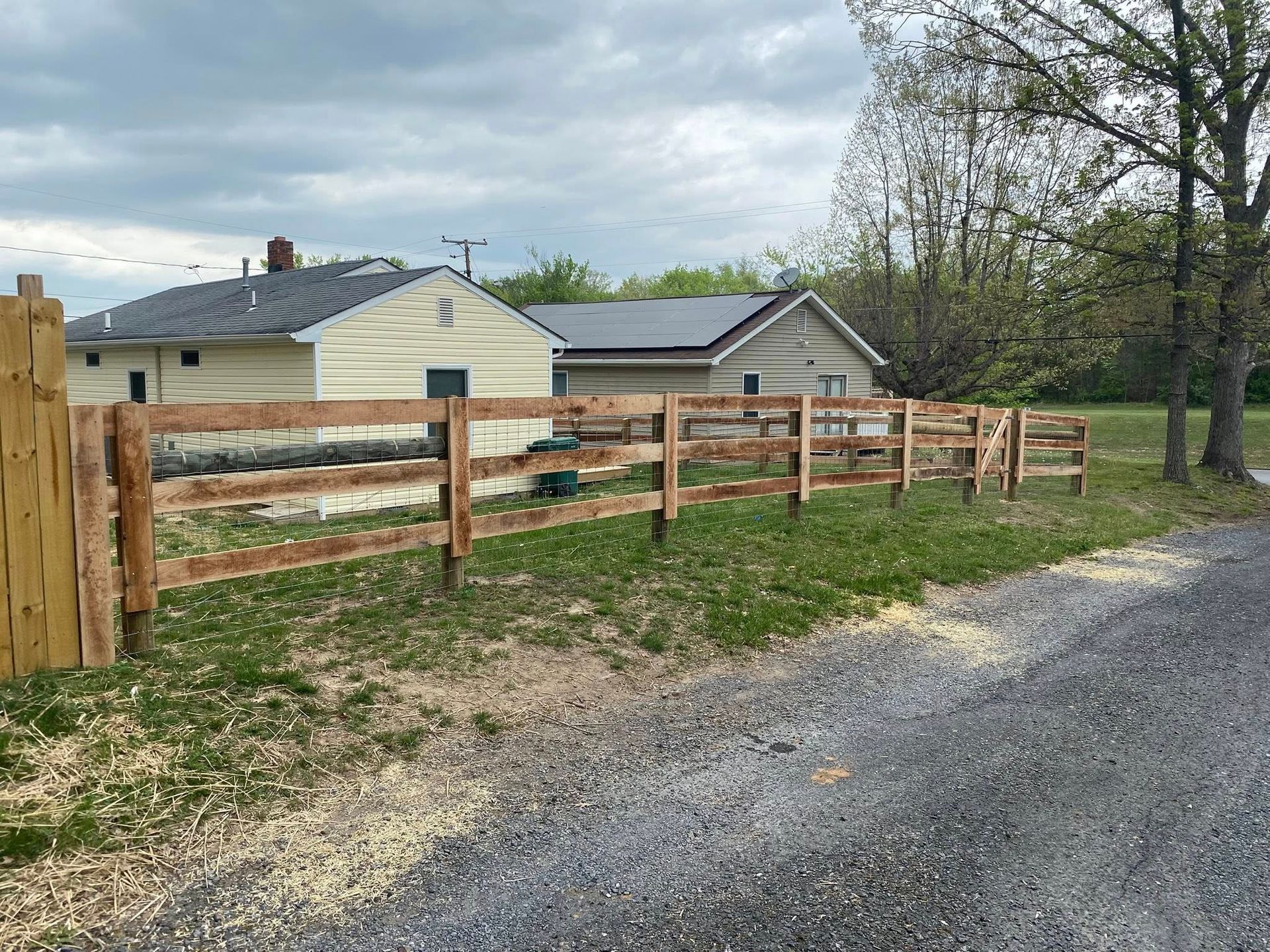 A wooden split-rail fence in front of two houses on a cloudy day.