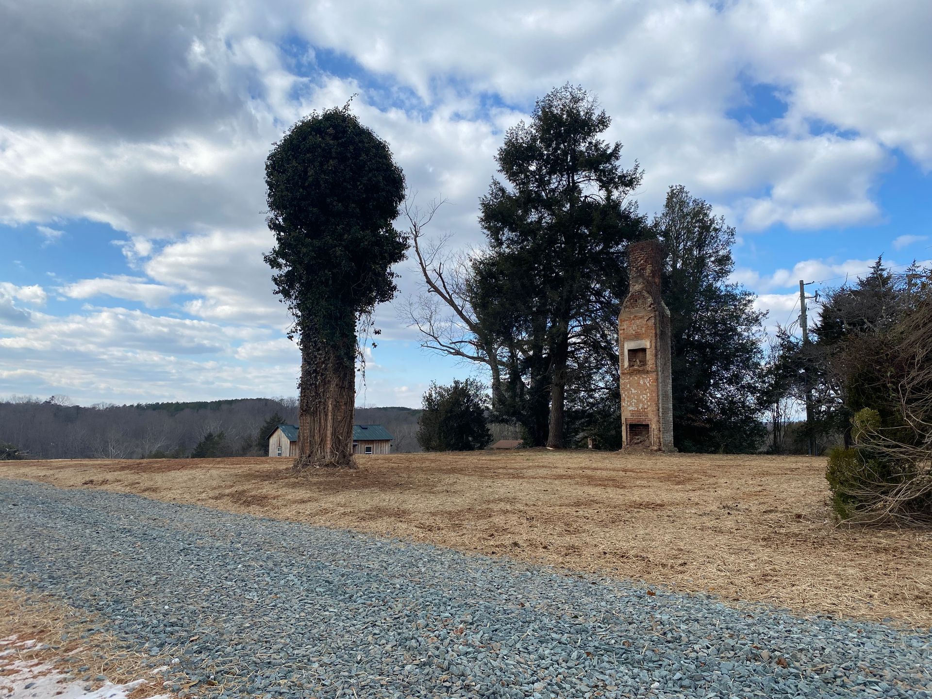 Overgrown brick chimney in a field of dry grass, under a cloudy sky.