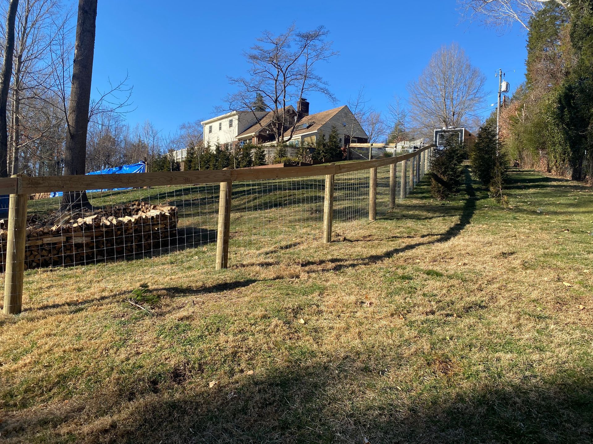 A wooden fence lines a grassy, sloped yard towards a house on a sunny day.