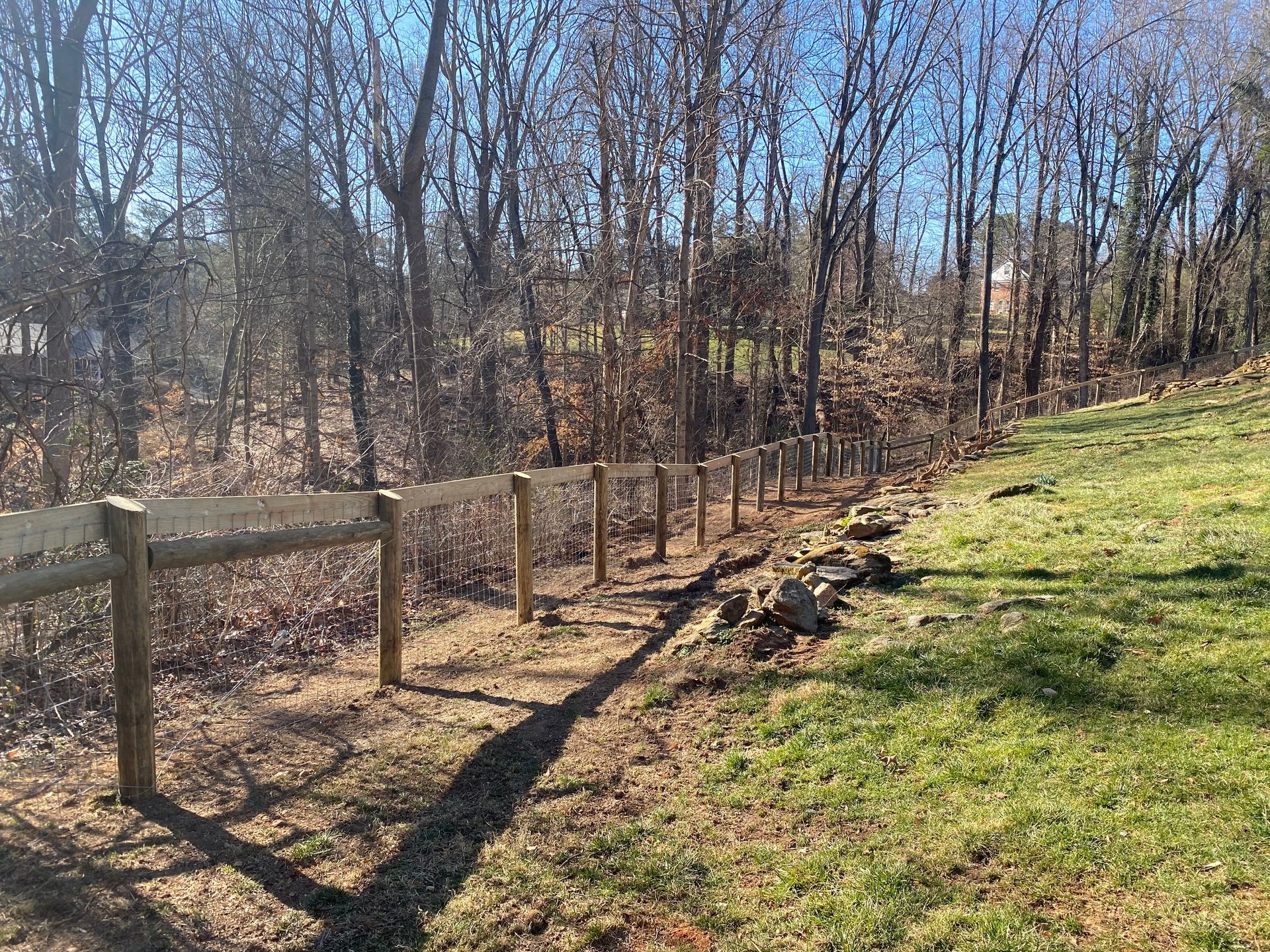 Wooden fence bordering a grassy area and a wooded area under a blue sky.