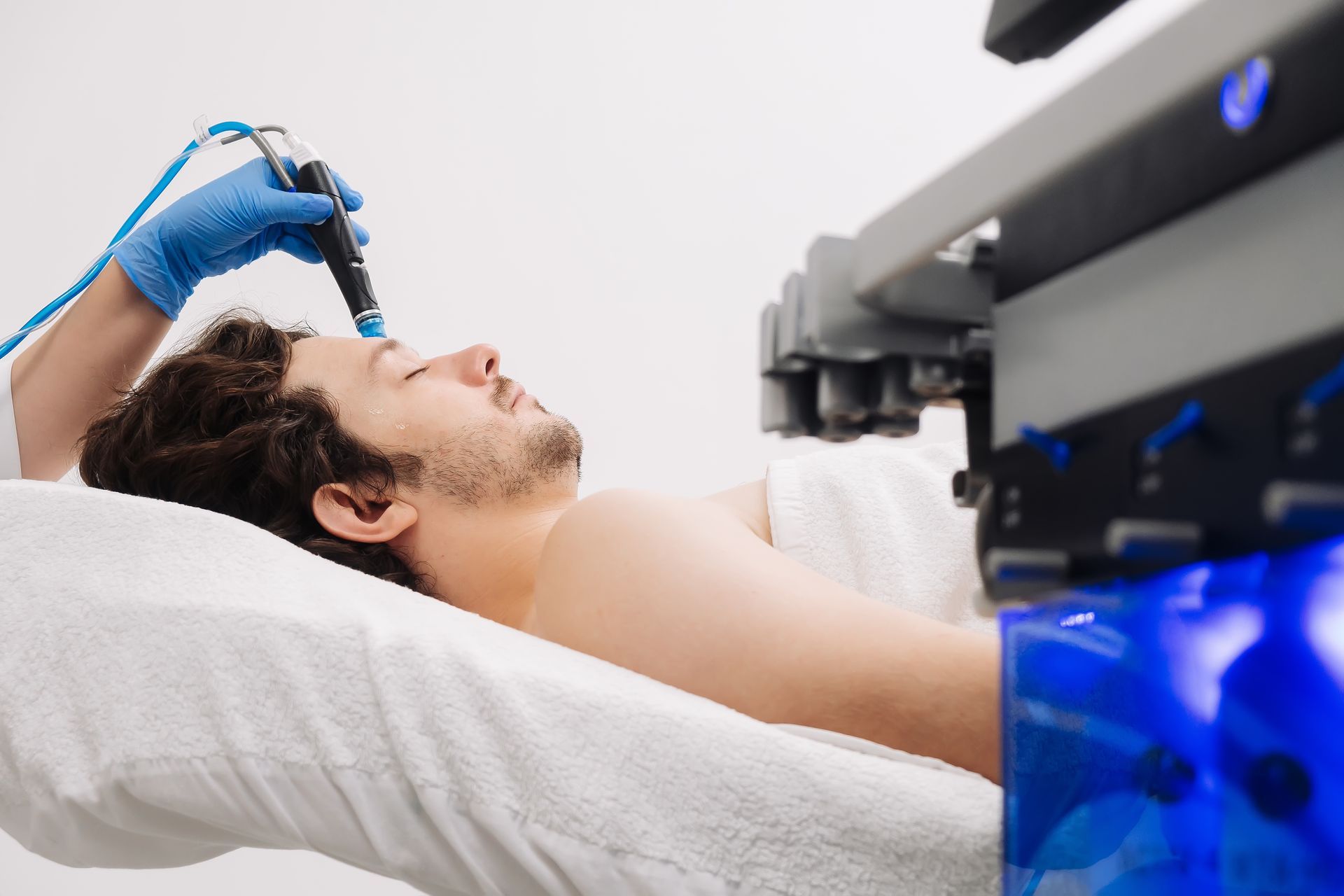 Woman receiving facial treatment, lying on a bed with closed eyes, hands holding cotton pads. Woman receiving facial treatment, lying on a bed with closed eyes, hands holding cotton pads.