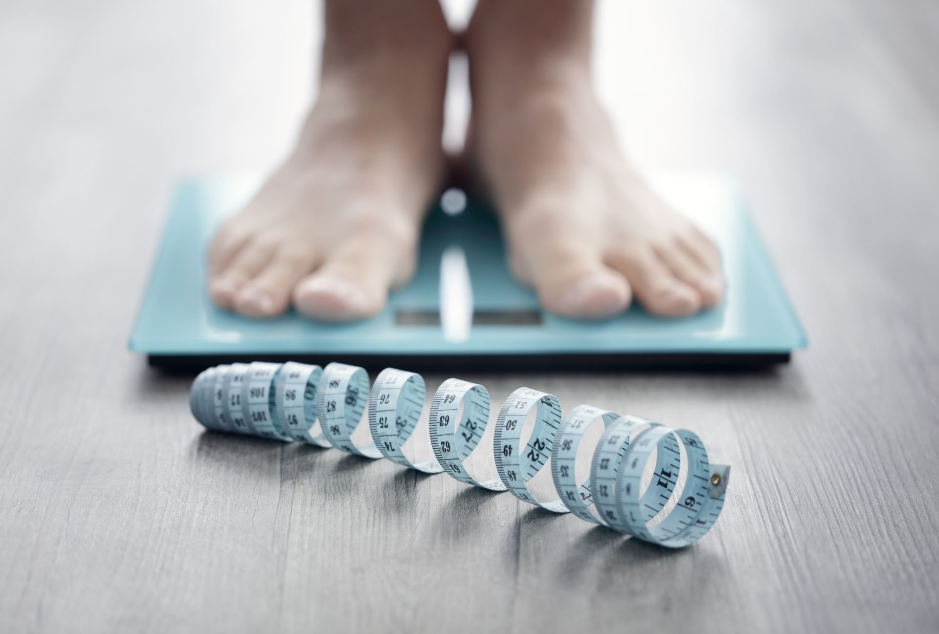 Feet on a scale, blue measuring tape on floor, potential weight loss theme.
