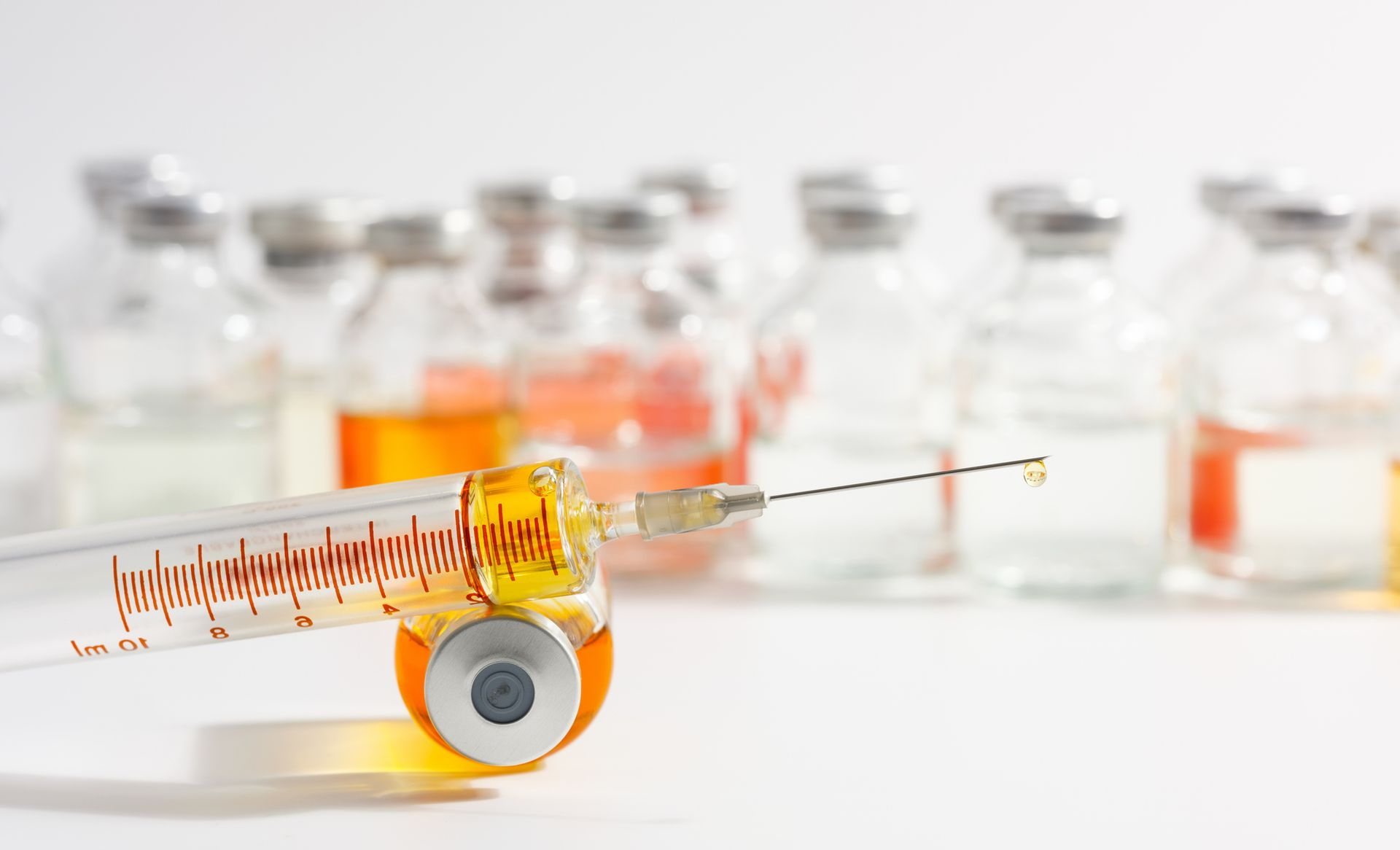 Syringe with needle next to a vial and cap, all on a pink surface.