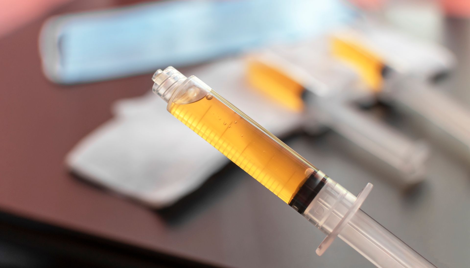 Syringe filled with yellow liquid, alongside two other syringes, on a table.