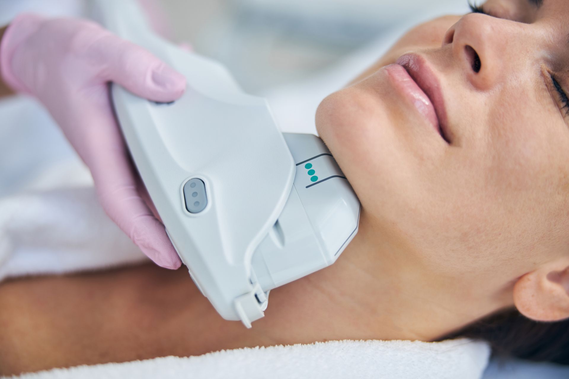 Woman undergoing skin tightening treatment on her neck with a handheld device.