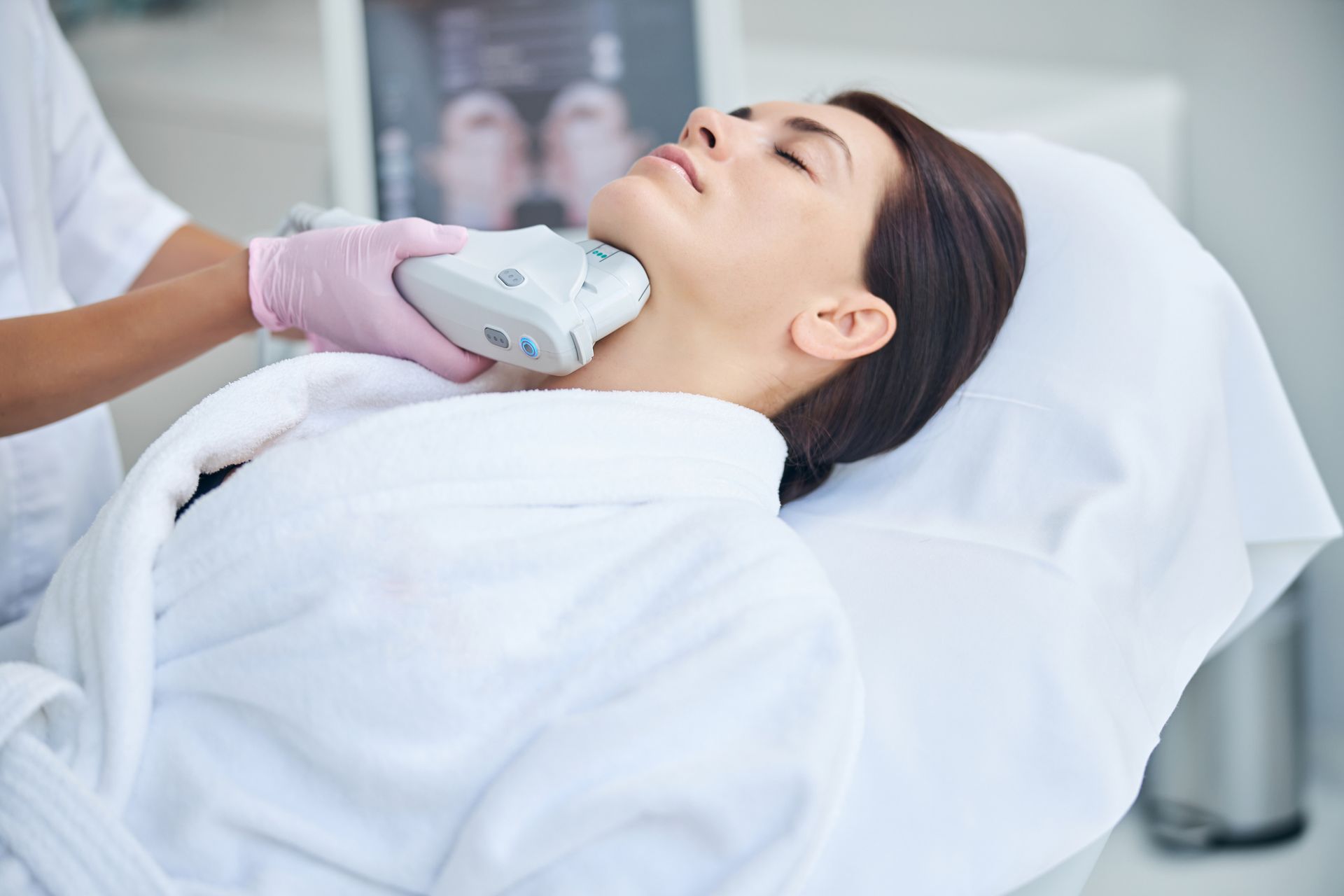 Woman receiving neck skin treatment in a clinic. Person in pink gloves operates device on her neck.
