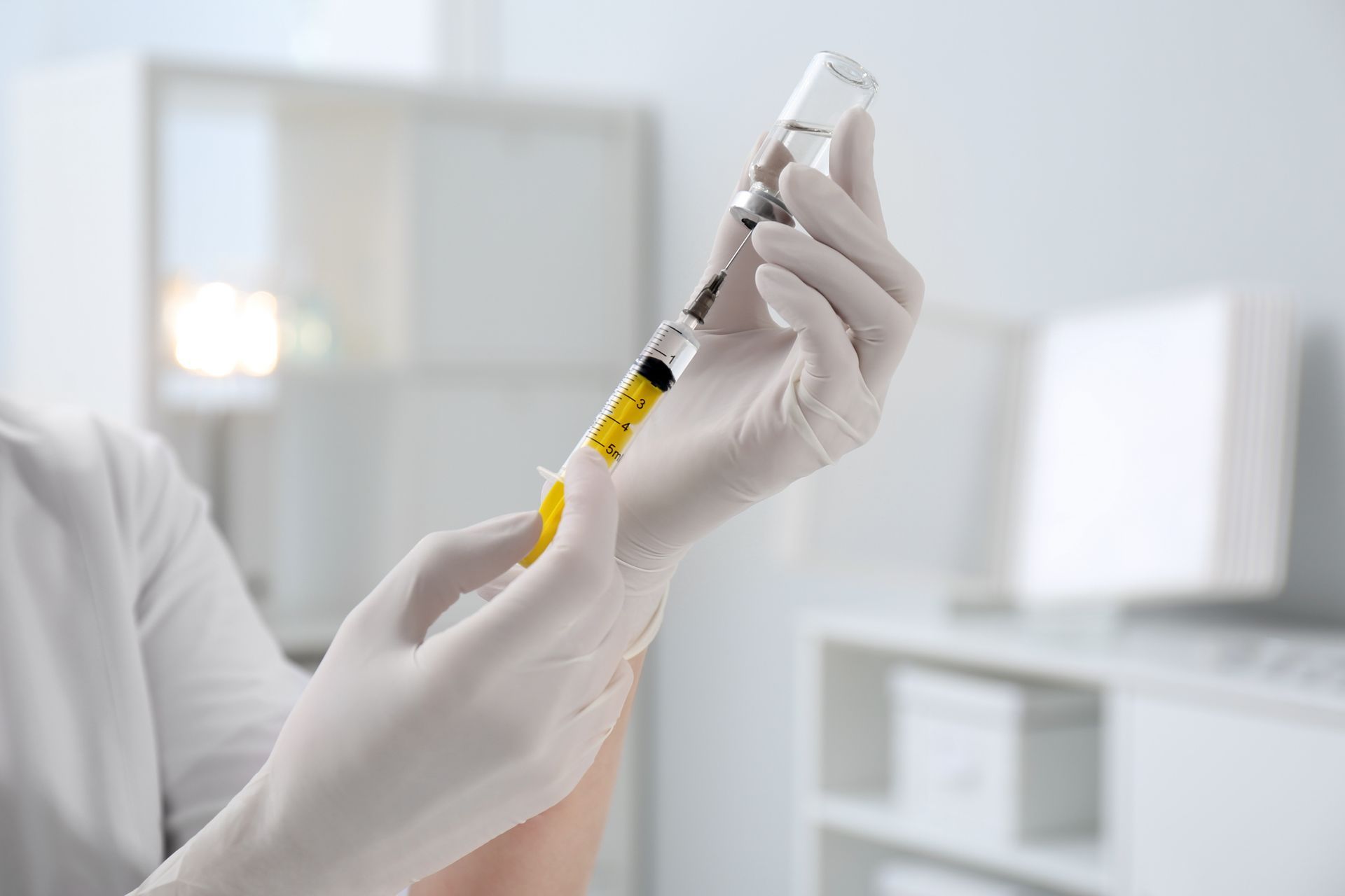 Person in white gloves drawing liquid from a vial with a syringe.