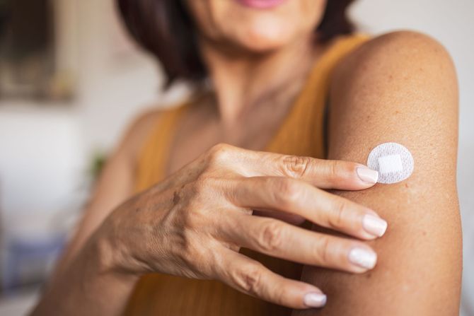 Woman applying a round, white patch to her upper arm.