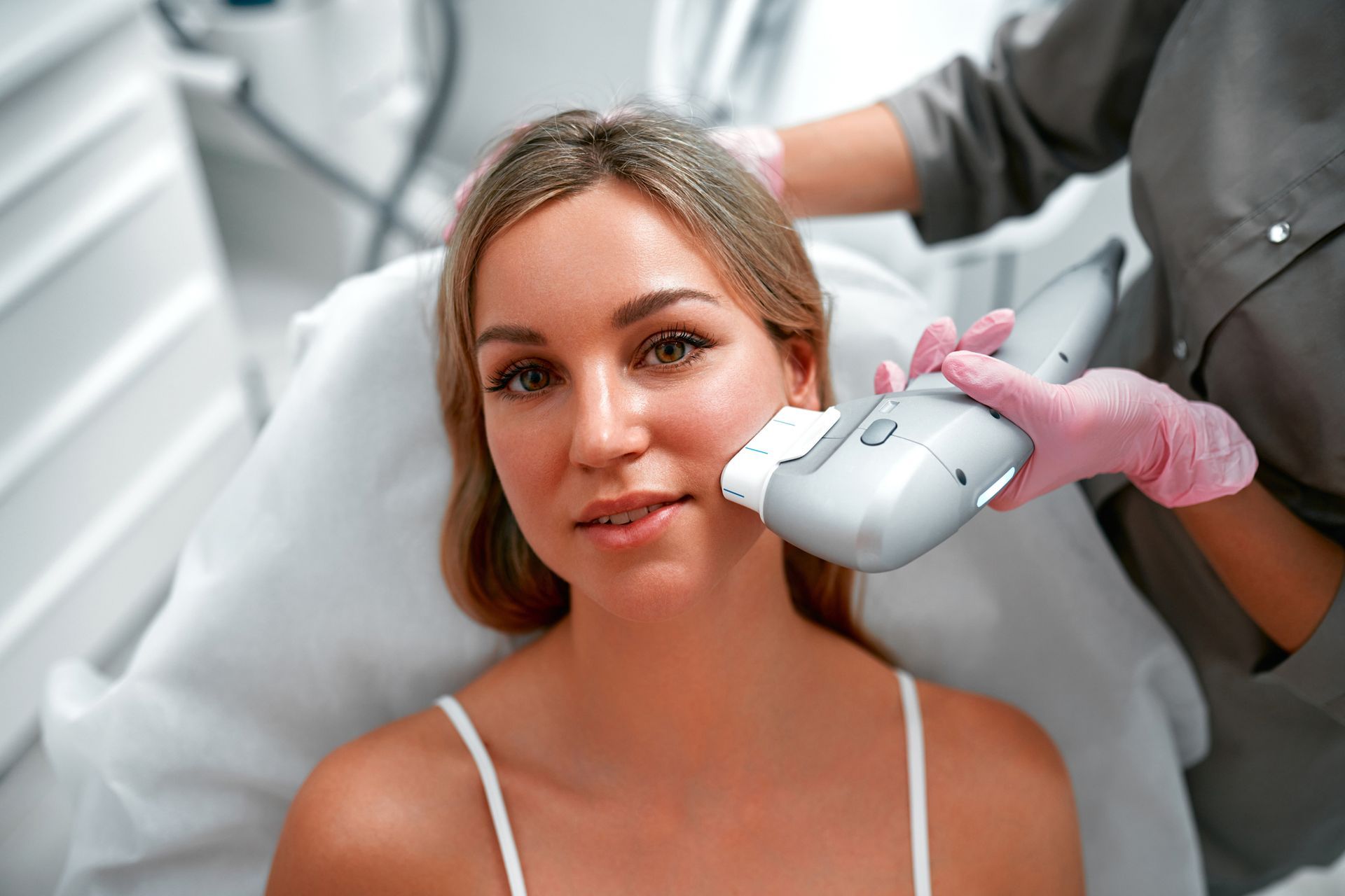 Woman receiving a facial treatment with a handheld device. Blonde hair, neutral expression, medical setting.