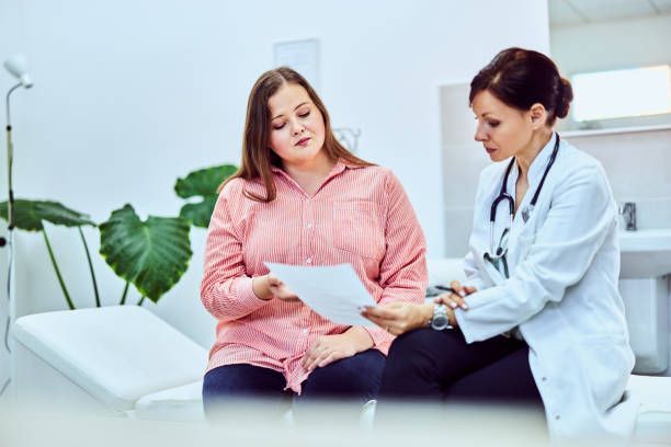 Woman in pink shirt reviewing paperwork with doctor in white coat.