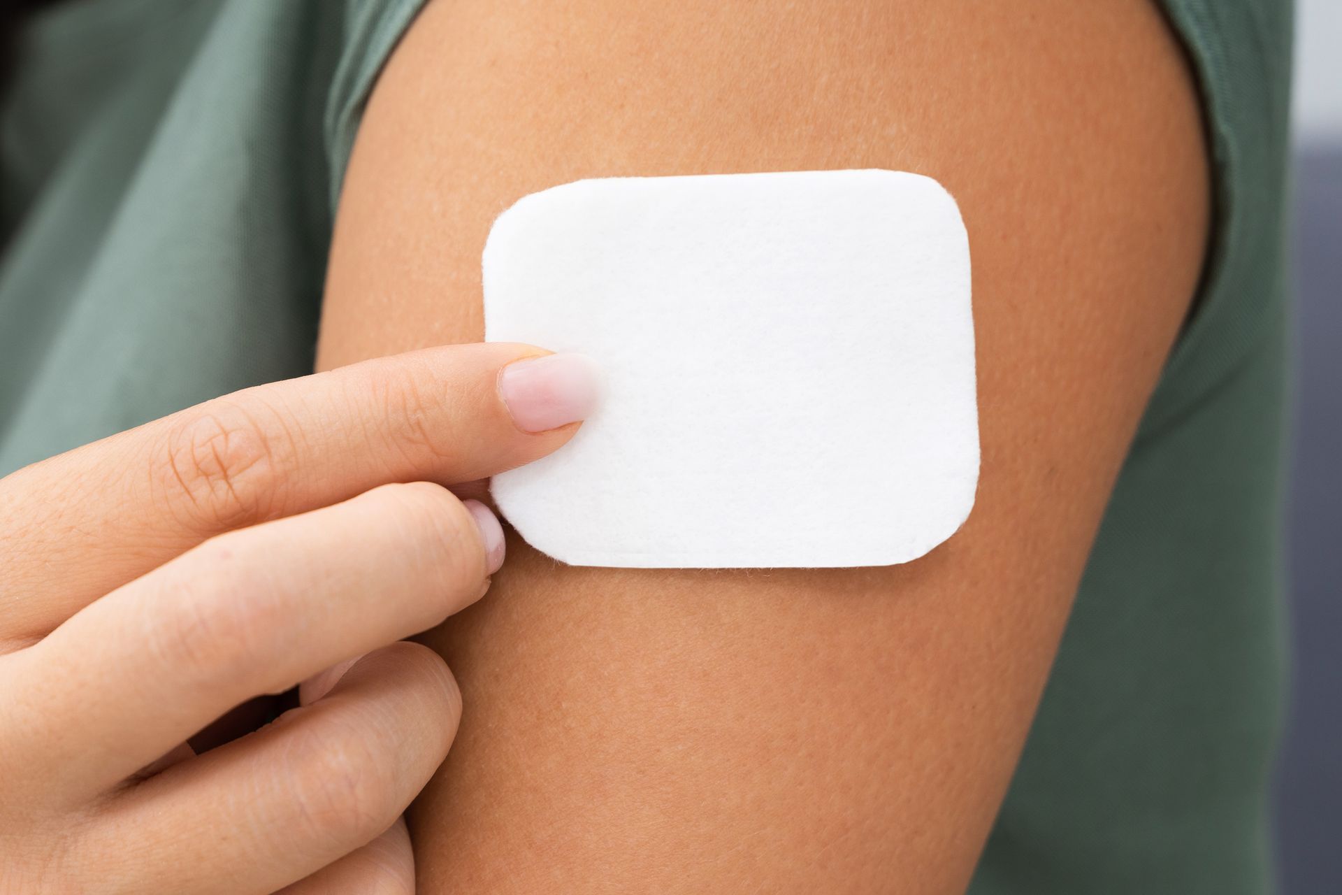 Woman's arm with a square, white patch applied. Hand holding the edge.