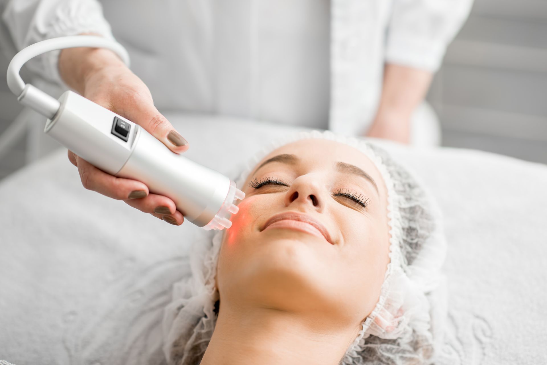 Woman receiving laser facial treatment in a spa setting; red light on face.
