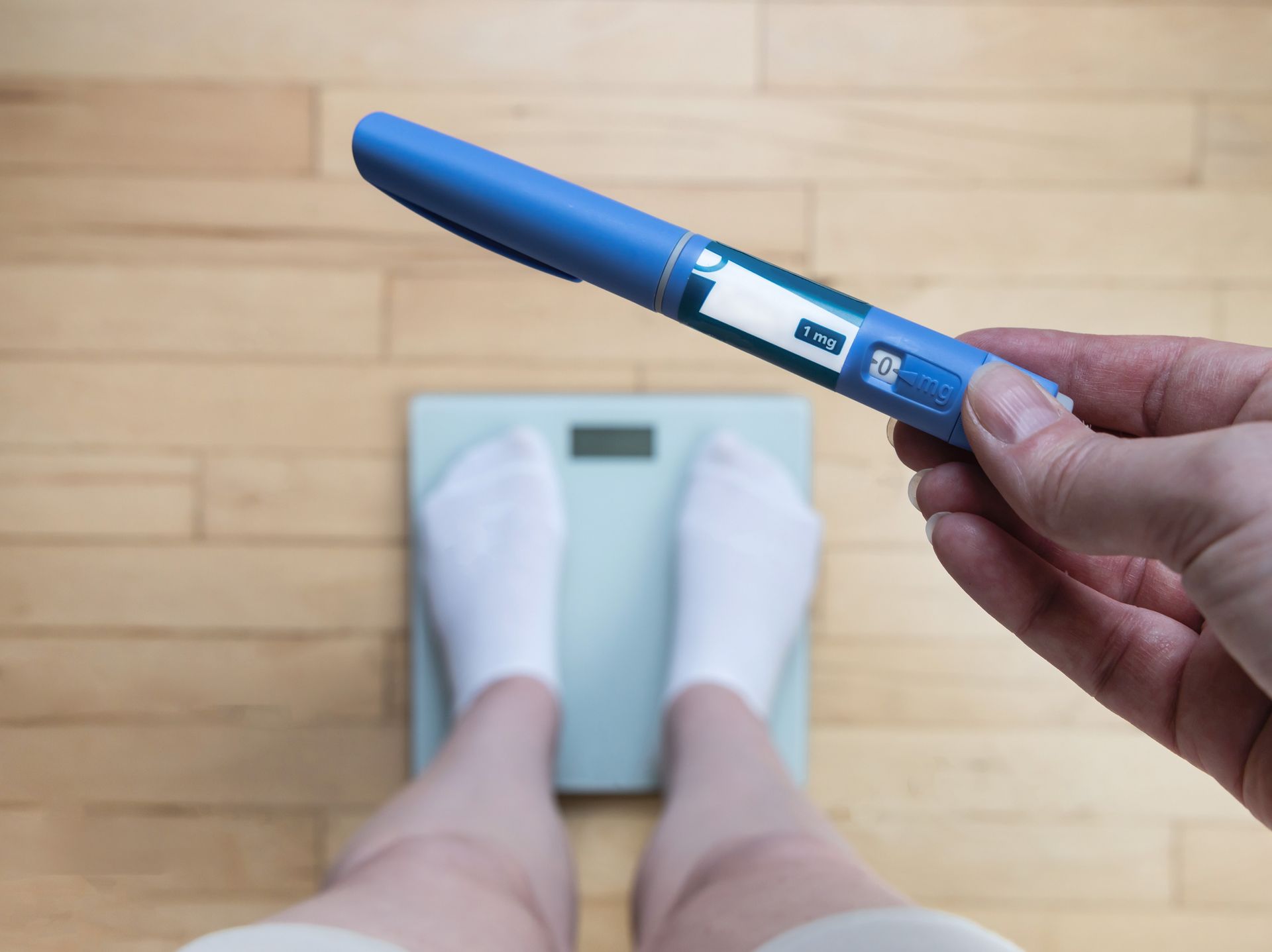 Person on scale with insulin pen; health and weight management.