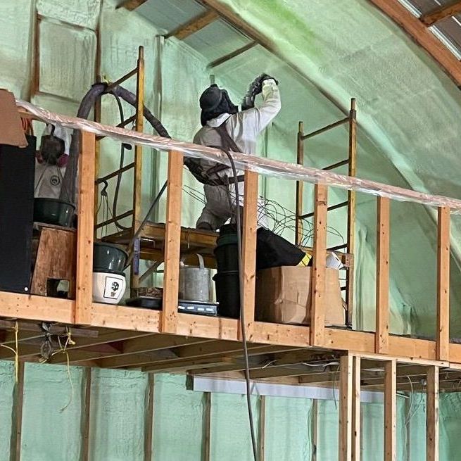 A man is spraying insulation on the ceiling of a building.
