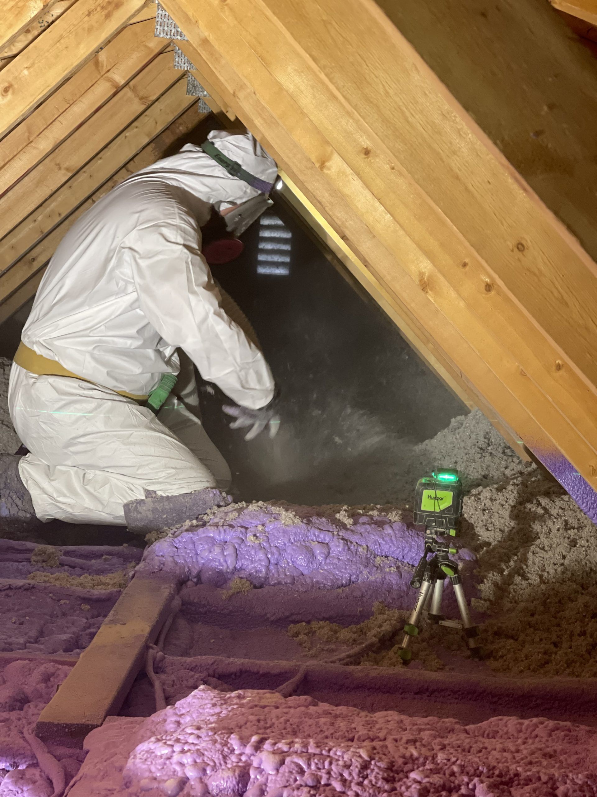 A man in a protective suit is working in an attic.