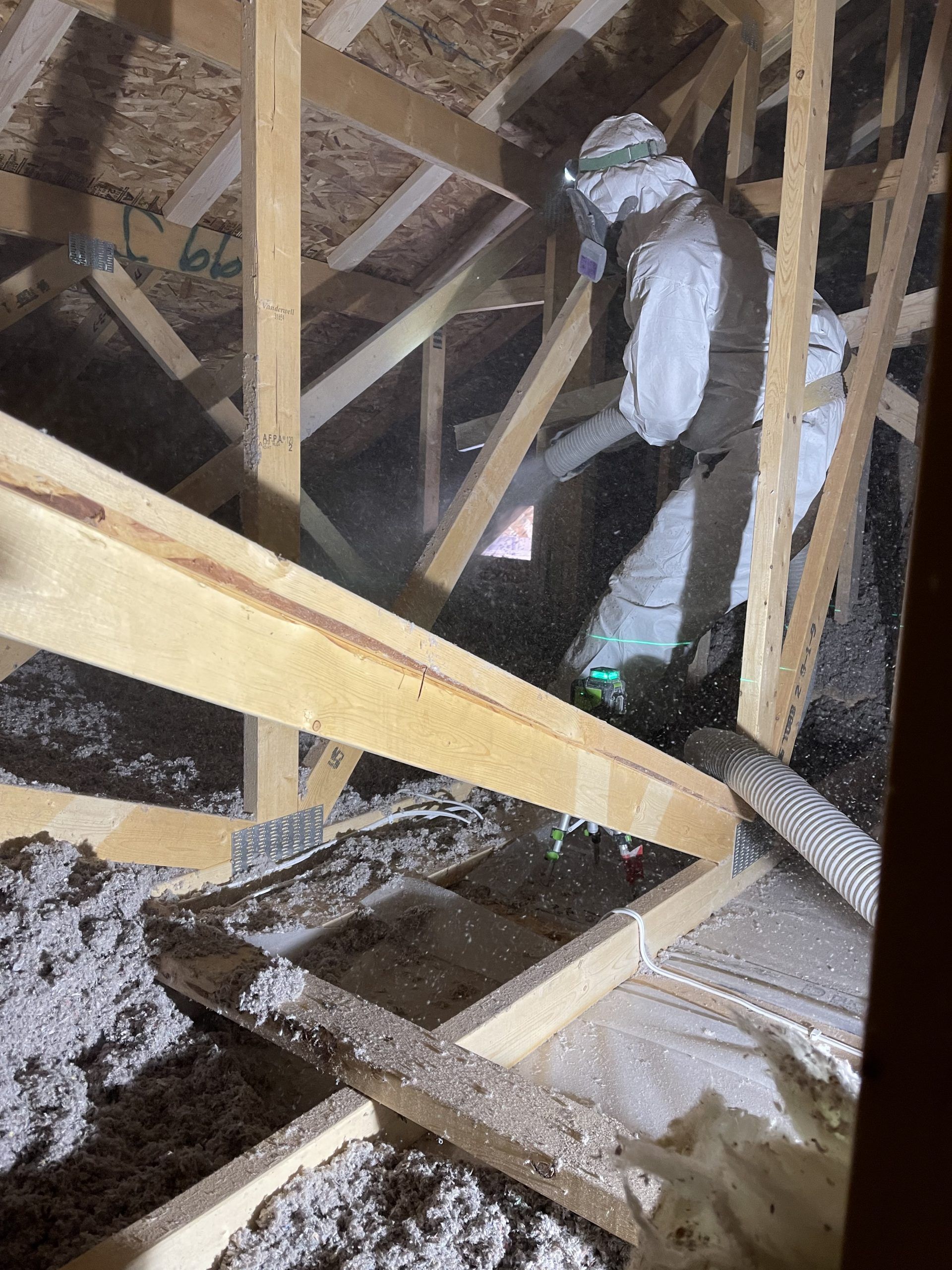 A man in a protective suit is spraying insulation in an attic.