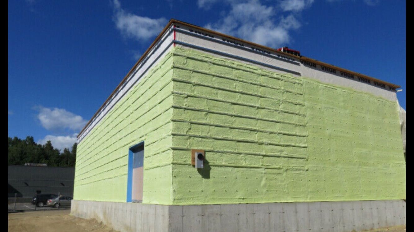 A man is spraying insulation on the ceiling of a building.